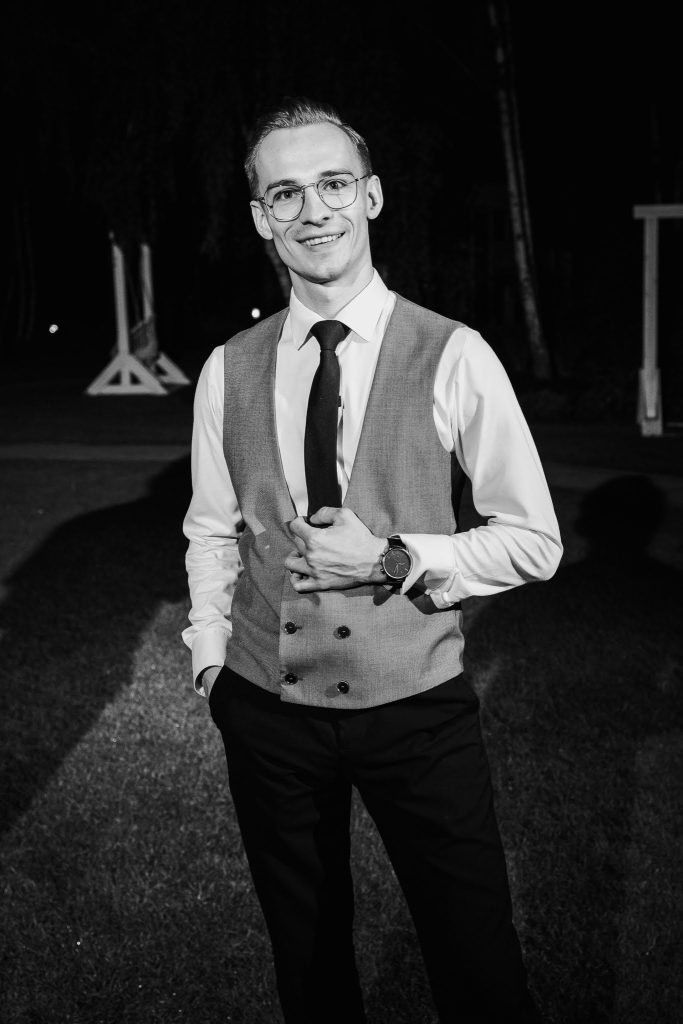 DJ Fuller w kamizelce i pod krawatem, portret czarno-biały, wieczorem przy sprzęcie.